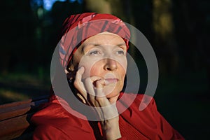 Female portrait of mature woman dressed in red clothes and sitting on the bench and enjoying a good weather and sunset