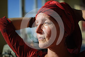 Female portrait of mature woman dressed in red clothes and sitting at the end of her work day on sewing machine and