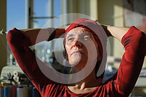 Female portrait of mature woman dressed in red clothes and sitting at the end of her work day on sewing machine and