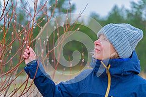 Female portrait outdoor. Pretty woman looking to pussy willow sallow bushes while walking in nature park in cold weather