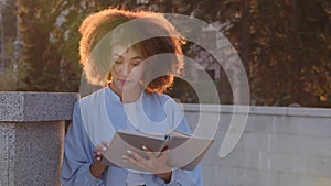 Female portrait outdoors african american lady girl student afro woman outdoor in sun sunlight reads book surprised