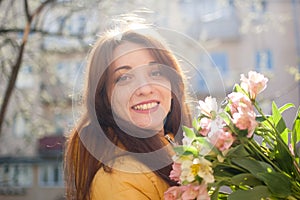 Female portrait of sensual brunette woman in yellow jacket holding a big bouquet of colorful flowers and looking at tne