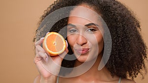 Female portrait studio smiling African American woman holding half fresh healthy orange fruit play with curly hair