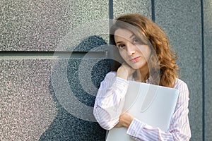 Female portrait of young woman with silver laptop, businesswoman is posing with digital tablet outside on dark wall