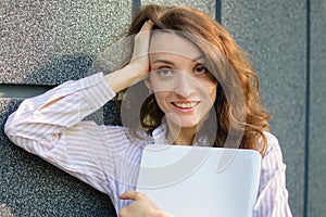 Female portrait of young woman with silver laptop, businesswoman is posing with digital tablet outside on dark wall