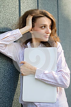 Female portrait of young woman with silver laptop, businesswoman is posing with digital tablet outside on dark wall