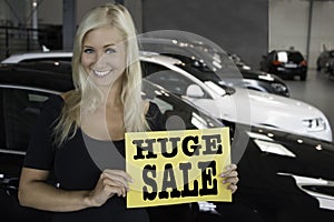 Female posing with sign in front of new cars