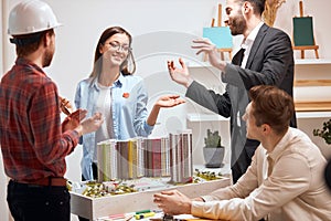 Female positive architect showing house model to smiling team in his office