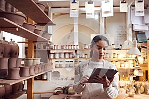 Female Potter In Ceramics Studio Checking Orders Using Digital Tablet