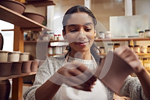 Female Potter Fitting Clay Handles To Mugs In Ceramics Studio