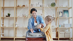 Female potter makes a pot on the pottery wheel with her daughter