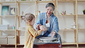 Female potter makes a pot on the pottery wheel with her daughter