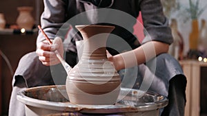 Female potter paints on rotating clay pot on the pottery wheel. Close up shot of potter making ceramic pot on pottery
