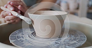 Female potter paints rotating pot on the pottery wheel.