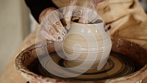 Female potter`s hands with red manicure working with wet clay on a pottery wheel making a clay product in a workshop