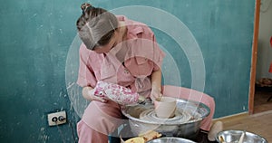 Female potter sitting and firing a shape cup clay on the pottery wheel. Woman making ceramic item. Pottery firing