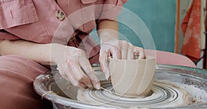 Female potter sitting and makes a cup on the pottery wheel. Woman making ceramic item. Pottery working, handmade and