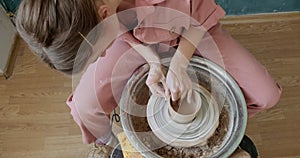 Female potter sitting and makes a cup on the pottery wheel. Woman making ceramic item. Pottery working, handmade and