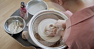 Female potter sitting and makes a cup on the pottery wheel. Woman making ceramic item. Pottery working, handmade and