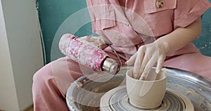 Female potter sitting and makes a cup on the pottery wheel. Woman making ceramic item. Pottery working, handmade and