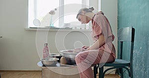 Female potter sitting and makes a cup on the pottery wheel. Woman making ceramic item. Pottery working, handmade and