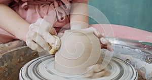 Female potter sitting and makes a cup on the pottery wheel. Woman making ceramic item. Pottery working, handmade and