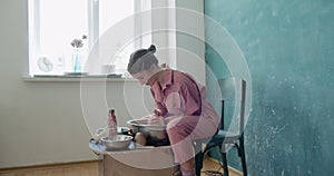 Female potter sitting and makes a cup on the pottery wheel. Woman making ceramic item. Pottery working, handmade and