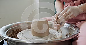 Female potter sitting and makes a cup on the pottery wheel. Woman making ceramic item. Pottery working, handmade and