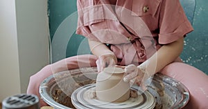 Female potter sitting and makes a cup on the pottery wheel. Woman making ceramic item. Pottery working, handmade and