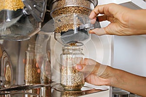 Female Pours Green Lentils from Vending Machine in a Glass Jar. Young Vegan Woman Shopping at Zero Waste Shop. No plastic