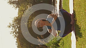 Female practicing yoga exercises on grass in park at sunset. Vertical video