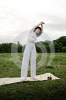 Female practicing yoga outdoor. Young sports woman retreat exercises. Asana coach hands to the slides on fresh air. Girl
