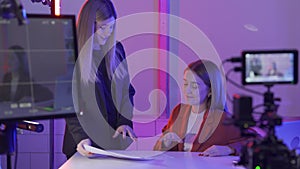 A female presenter discusses a storyboard with a female producer before filming begins in close up. Women in a studio in