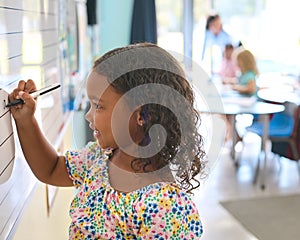 Female Primary Or Elementary School Student Writing On Whiteboard In Classroom Lesson