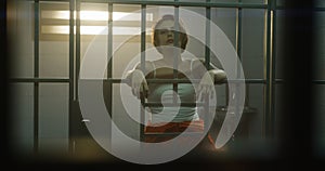 Female prisoner stands in jail cell, looks at camera