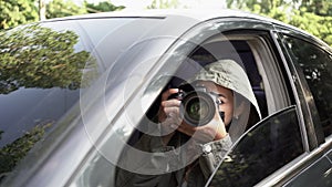 Female private detective or paparazzi with a camera sit in a car, takes photo of object of surveillance.