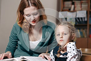 Female private tutor helping young student with homework at desk in bright child`s room