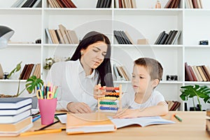 Female private tutor helping young student with homework at desk in bright child`s room