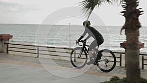 Female pro cyclist is cycling on road aero bike on promenade. Woman athlete is training on bicycle and preparing for competition r