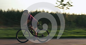 Female pro cyclist is hard pedaling on road aero bike at sunset. Woman athlete is training on bicycle and preparing for competitio