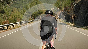 Female pro cyclist hard pedaling on road bike in mountains. Woman athlete training on bicycle and preparing for competition race.