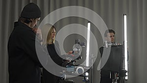 Female producer, camera operator and lighting technician in the studio during filming. The lighting technician adjusts