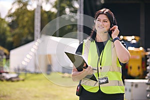 Female Production Worker Talking On Headset Setting Up Outdoor Stage For Music Festival Or Concert