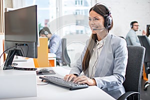 Female professional call center telesales agent using computer in customer care support service office with team.