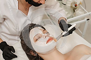 Female professional cosmetologist& x27;s hands applying mask to patient& x27;s face for facial skin care. Female client