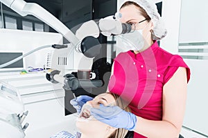 A female professional dentist examines a female patient with a stamotologic microscope in her office. Stamotologist