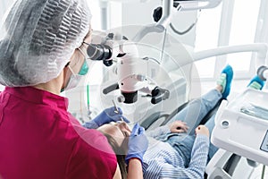 A female professional dentist examines a female patient with a stamotologic microscope in her office. Stamotologist