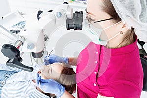 A female professional dentist examines a female patient with a stamotologic microscope in her office. Stamotologist