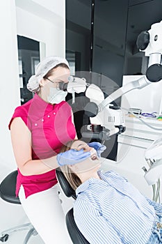 A female professional dentist examines a female patient with a stamotologic microscope in her office. Stamotologist