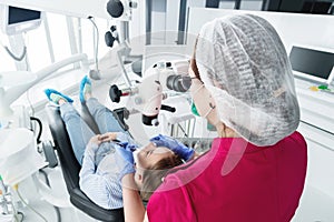 A female professional dentist examines a female patient with a stamotologic microscope in her office. Stamotologist